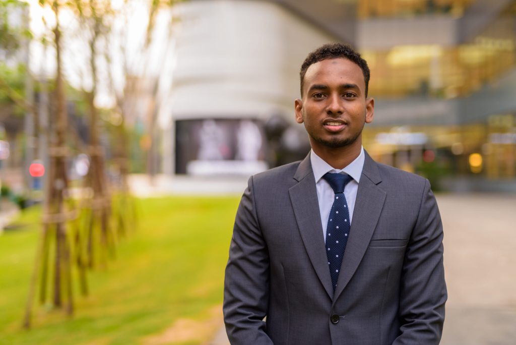 Young ethnic businessman in suit standing in front of a building